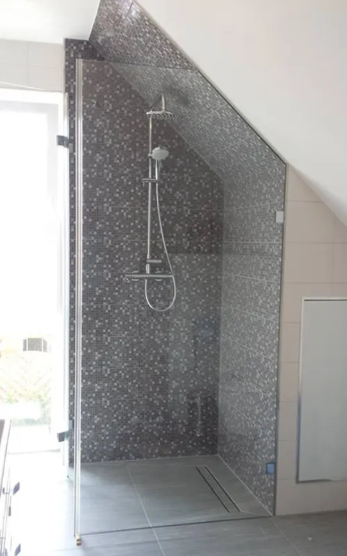 Walk-in shower under a sloping ceiling in front of a mosaic wall