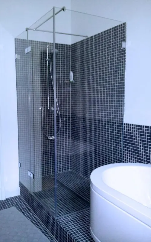 Corner shower next to the bath in front of dark mosaic