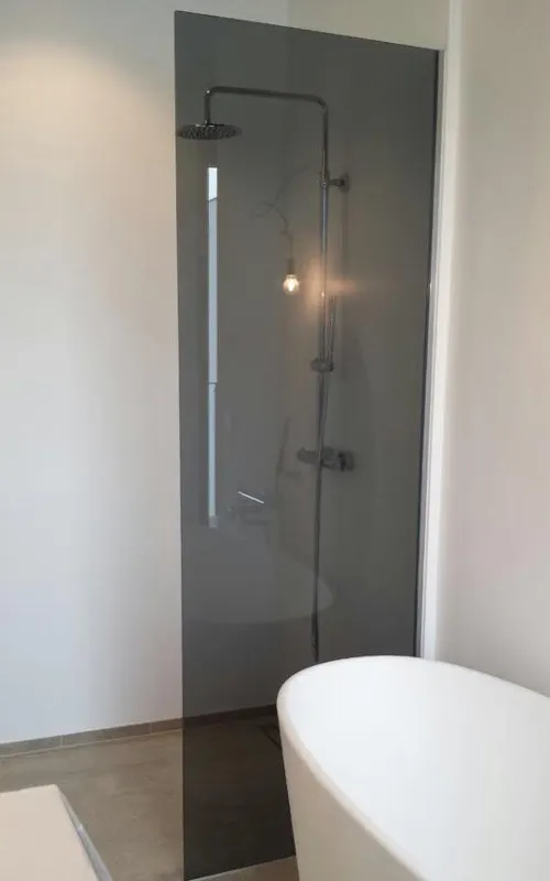 Walk-in glass wall in grey glass next to a freestanding bath