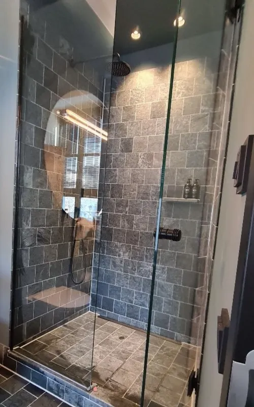 Frameless shower in toughened safety glass with black pivot door fittings in front of a natural stone wall