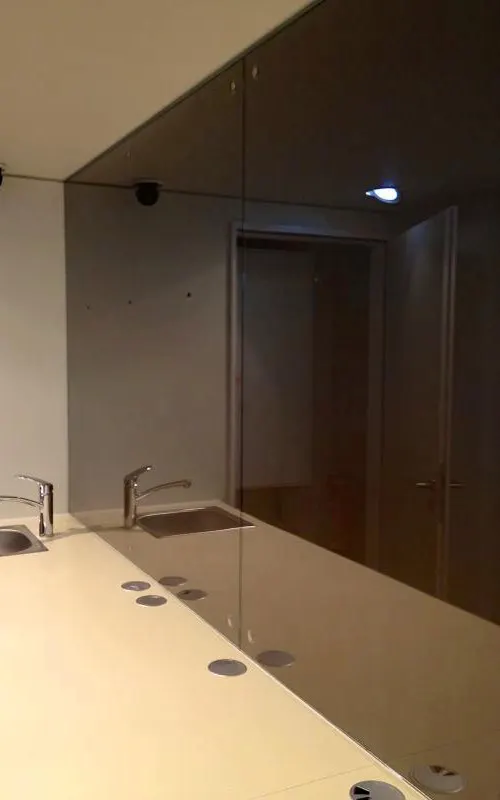 Wall in dark brown lacquered glass behind a light worktop with two basins