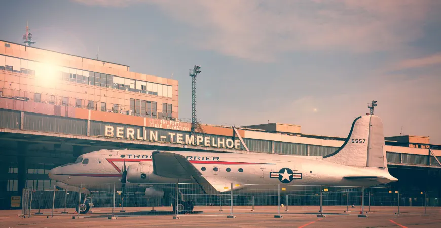 Flughafengebäude Berlin-Tempelhof mit Schriftzug, davor ein historisches Flugzeug auf dem Vorfeld