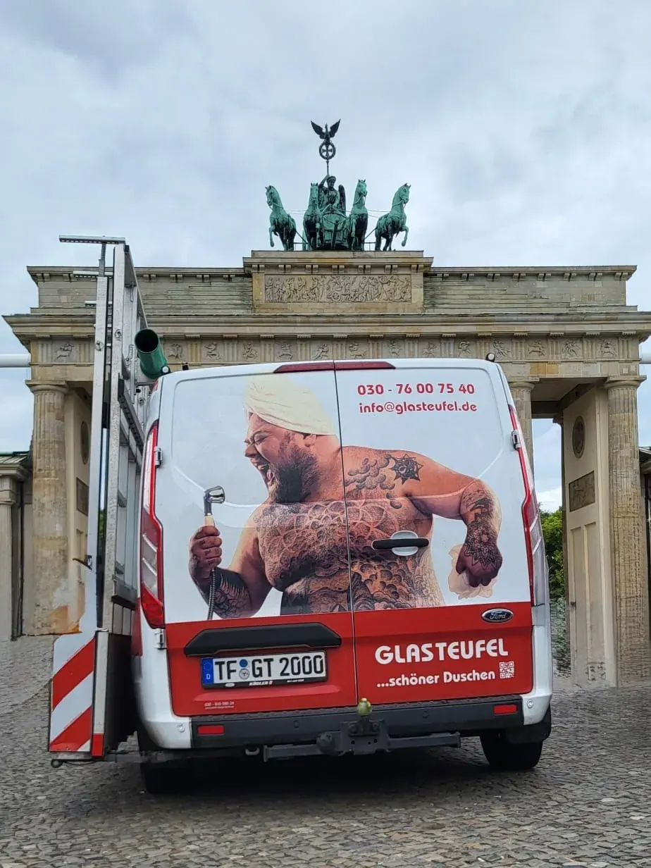 Montagefahrzeug von Glasteufel von hinten vor dem Brandenburger Tor: Hecktüren mit Werbemotiv und dem Schriftzug „Glasteufel …schöner Duschen“, seitlich ein Gestell für den Glastransport